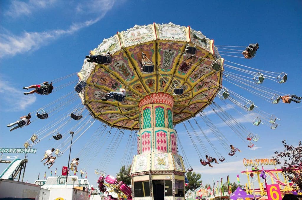 Riders enjoy a swing ride, round and round, at Calgary Amusement Park on a clear, blue day, one of the best vacation destinations for families In Canada.