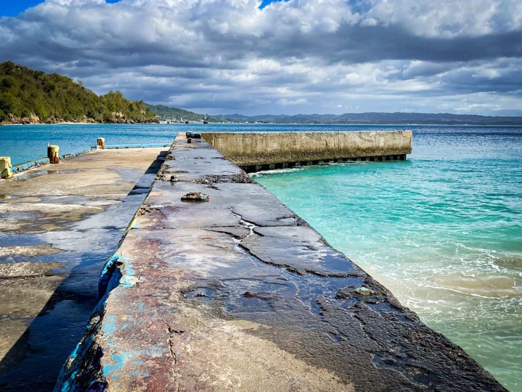 A stone pier reaches out into the water on a sunny day at Crash Boat Beach.