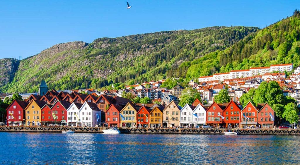A row of colorful homes along the water with green hills in the distance in Bergen, one of the best mild weather European destinations for a family summer vacation.