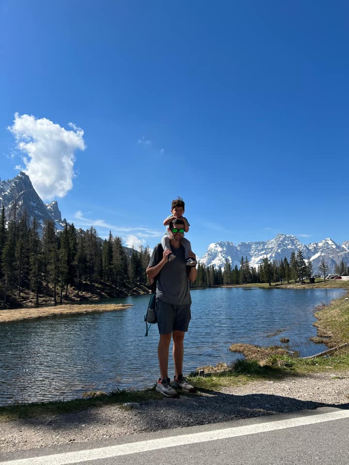 A dad holds his young son on his shoulders with Lake Como behind them.