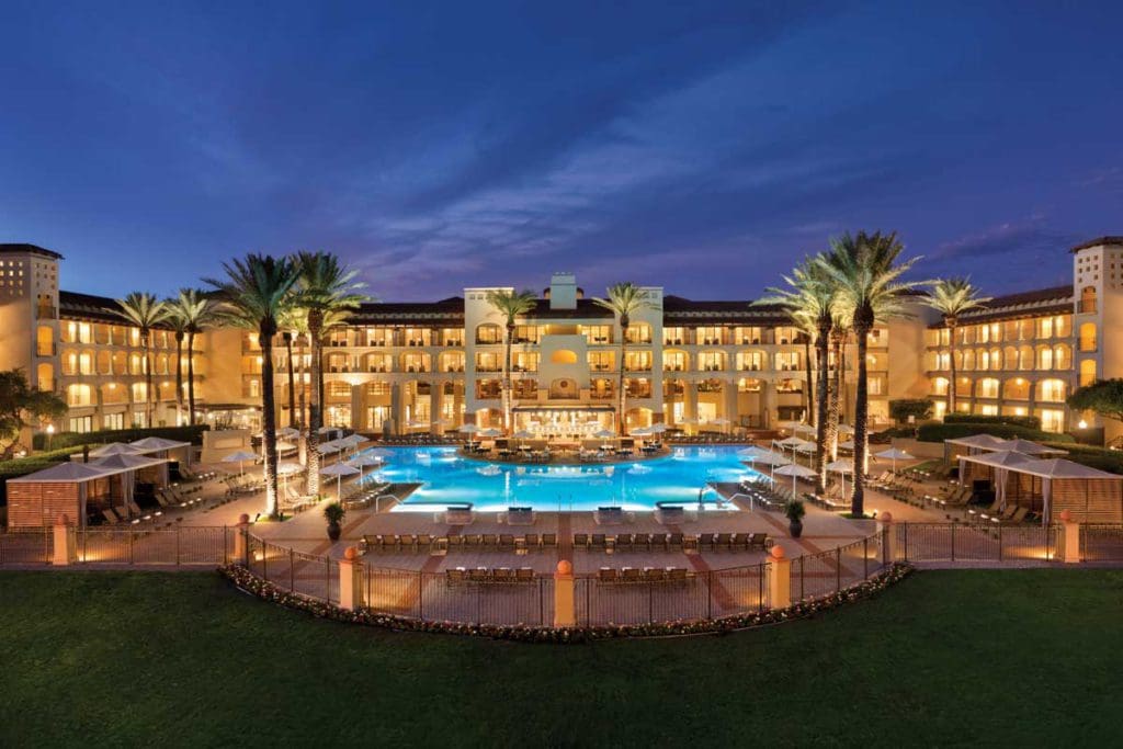 A wide shot of the outdoor pool, framed by palm trees and illuminated by the night sky, at the Fairmont Scottsdale Princess.