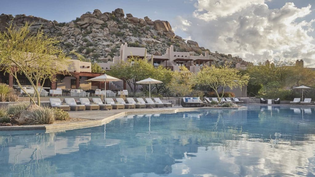 A view of the outdoor pool at the Four Season Resort Scottsdale, framed by lounge chairs and stunning rock scenery. This is one of the best luxury hotels in the U.S for families.