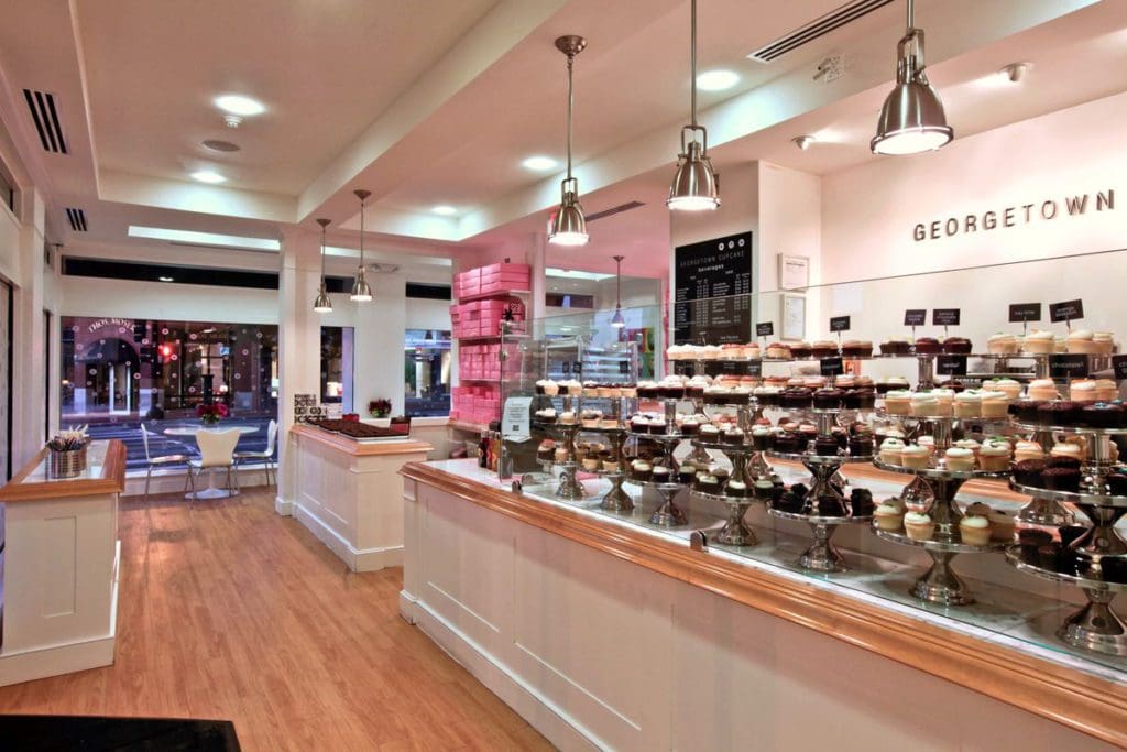 Inside Georgetown Cupcake, featuring a long line of gourmet cupcakes on the counter at one of the best dessert spots in DC for families.