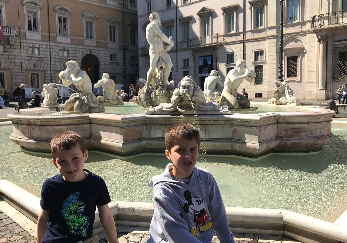 Two pose sit at the edge of a fountain on one side of Piazza Navona.