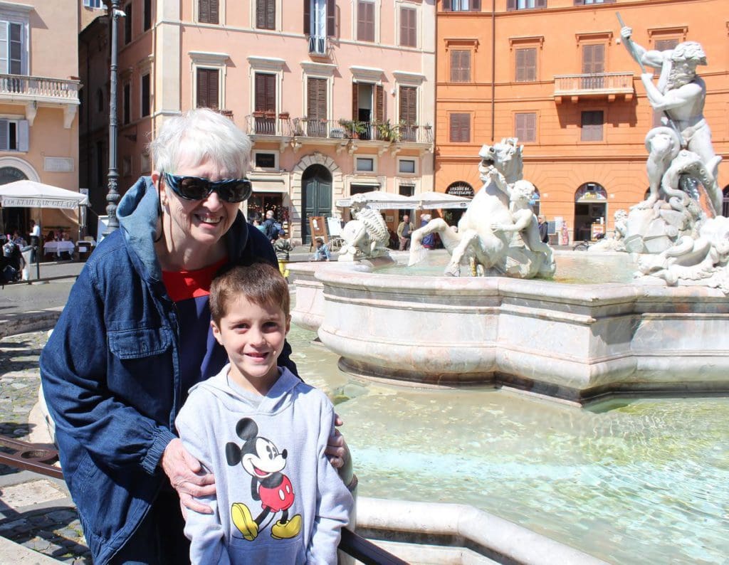 A grandmother and her grandson pose in front of one of the fountains in Piazza Navona.