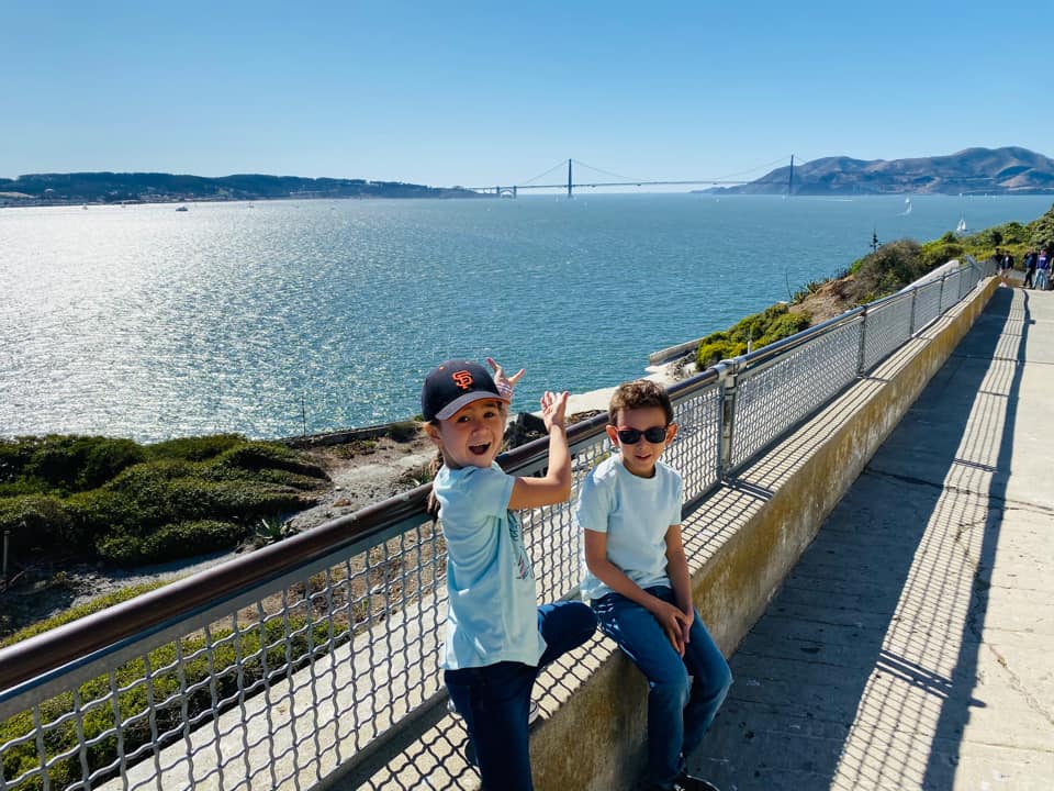 Two kids stand together enjoying a view of San Francisco and the Golden Gate Bridge from Alcatraz Island.