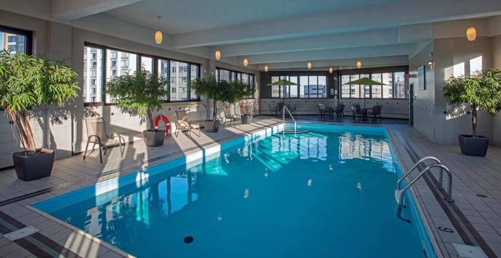 The indoor pool at , L'Appartement Hôtel, with floor to ceiling windows, indoor plants, and surrounding pool deck.