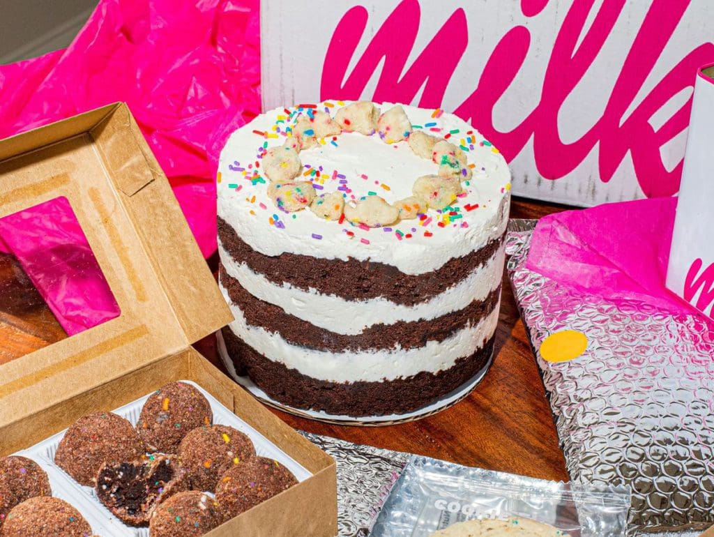 A tabled filled with a desserts, including a gourmet cake, and boxes featuring the Milk Bar logo.