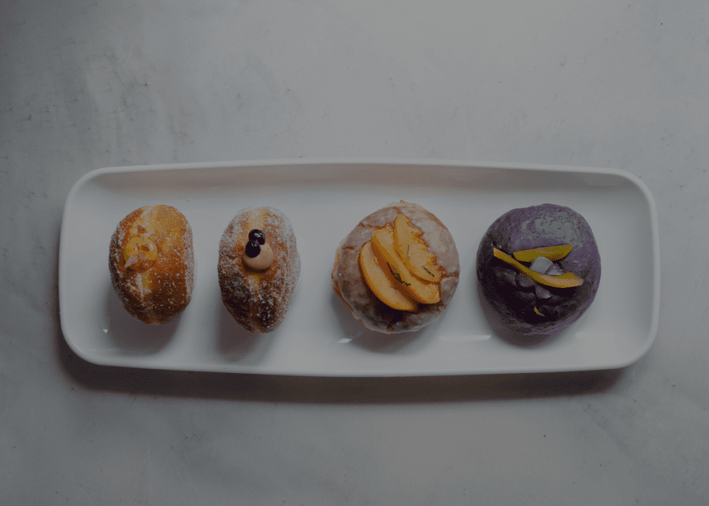 A white plate with four filled gourmet donuts on it from Rose Ave Bakery. 