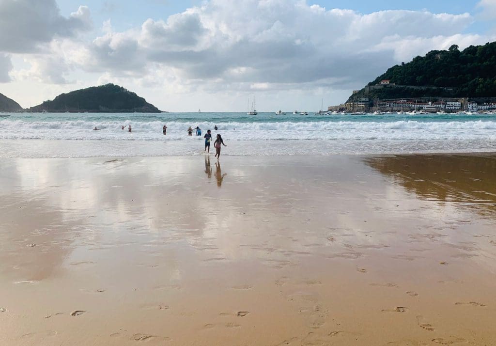 Kids run across the beach, with the water behind them, in San Sebestiaon.