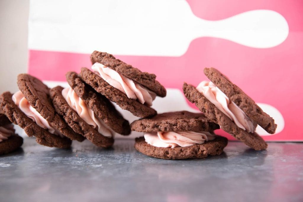 A row of gourmet cookie sandwiches, with chocolate cookies and pink frosting, at Sticky Fingers Sweets & Eats.