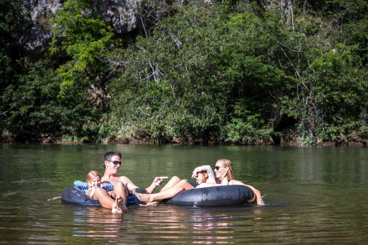 A family of four floats along a river in black inner-tubes at Sweet Songs Jungle Lodge, a Muy’Ono Resort.