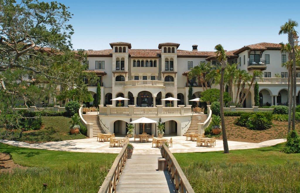Front view of The Cloister at Sea Island, featuring a paved path shaded by trees and grass. 