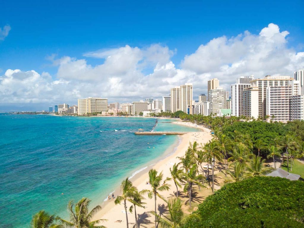 An aerial view of an empty Waikiki Beach, with a stretch of hotels lining the far shore.