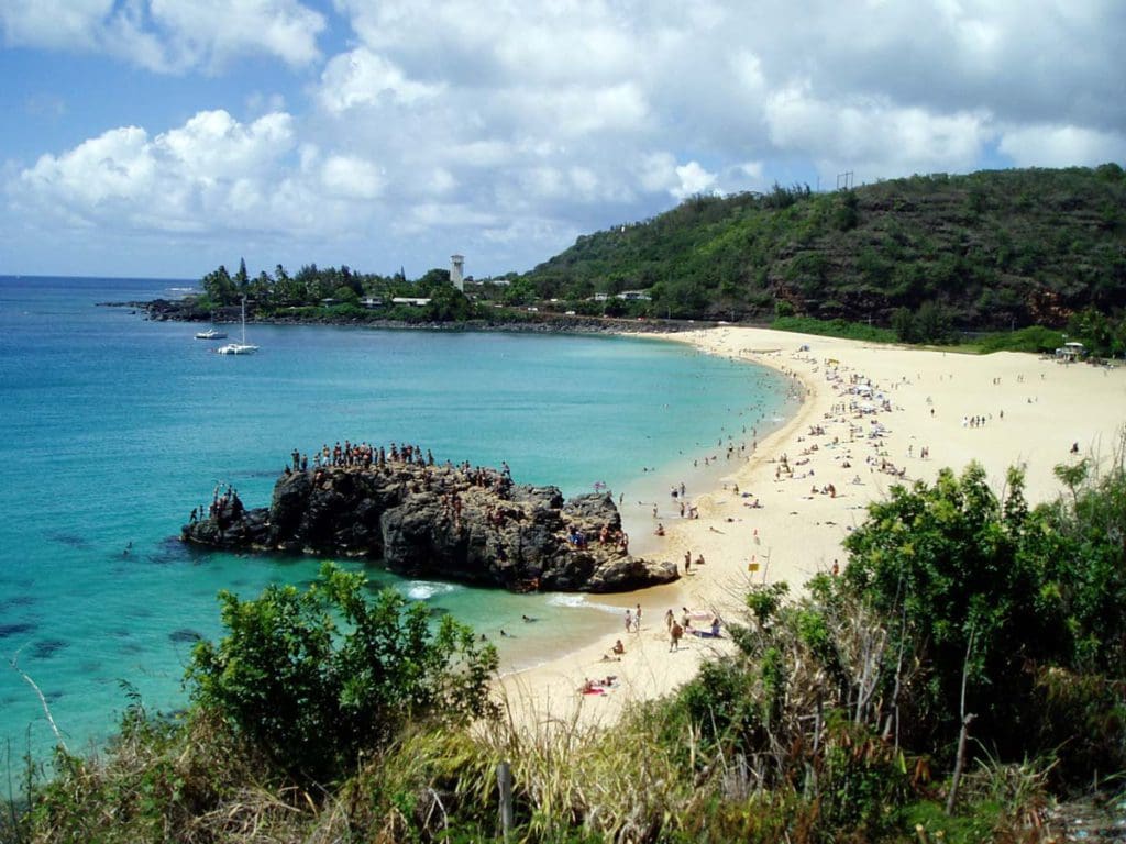 An aerial view of Waimea Bay, featuring a long stretch of white sand beach and turquoise waters.