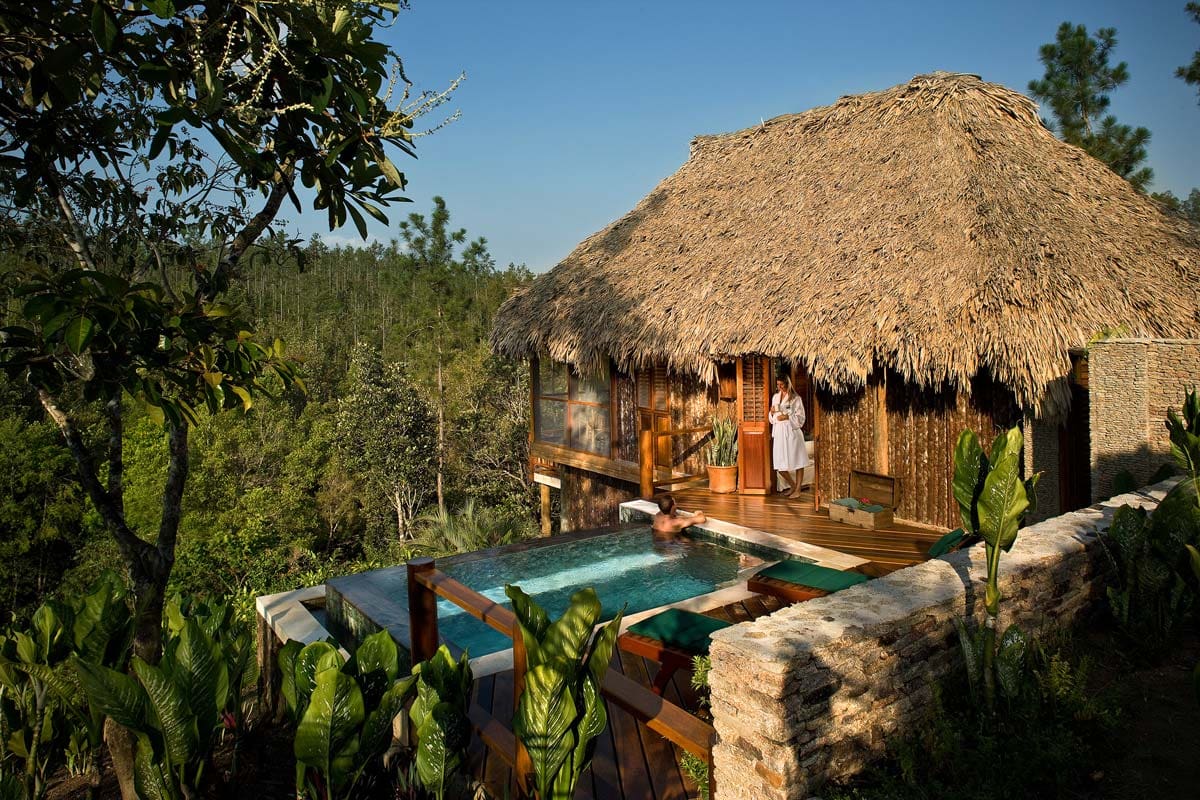 A woman stands in the doorway of her accommodation at Blancaneaux Lodge, with a pool and lush surroundings. 