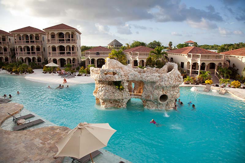 The fun pool at Coco Beach Resort, featuring a stone structure in the center and resort buildings flanking one side.