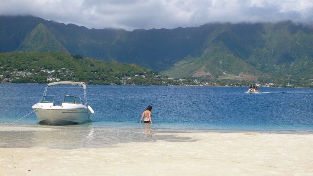 A woman wades hip-deep in the water near a boat in Kaneohe Bay Sandbar.