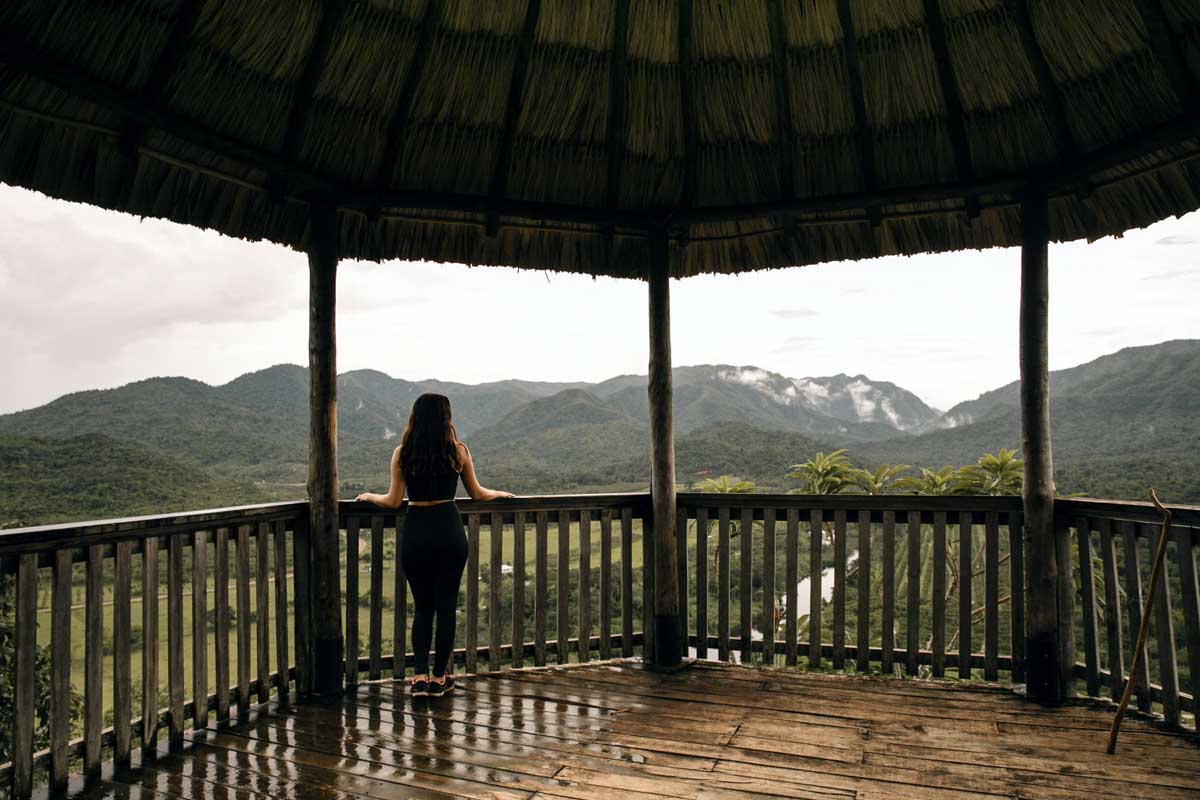 A woman stands at the edge of a terrace looking out at the rain forest and nearby mountains at Sleeping Giant Rainforest Lodge.