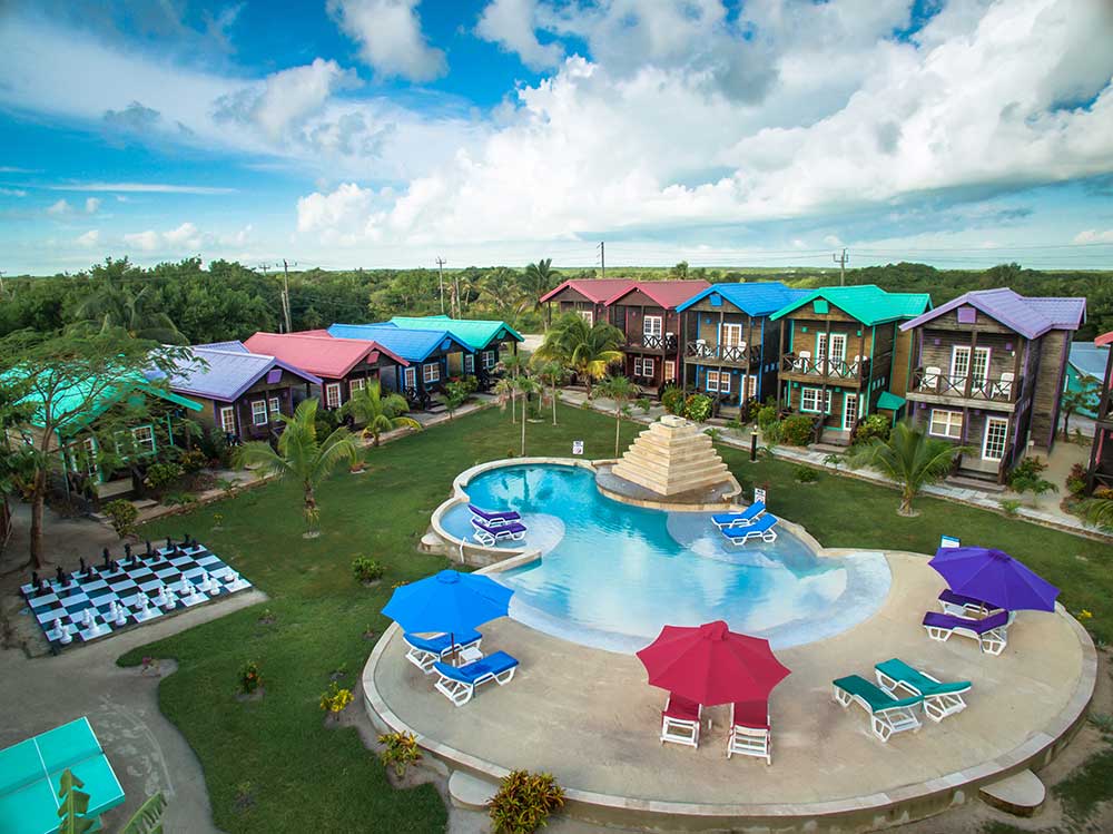An aerial view of the intimate pool and nearby life-size chess game, with resort buildings flanking the lawn, at X’Tan Ha Resort one of the best Belize resorts for a family vacation.