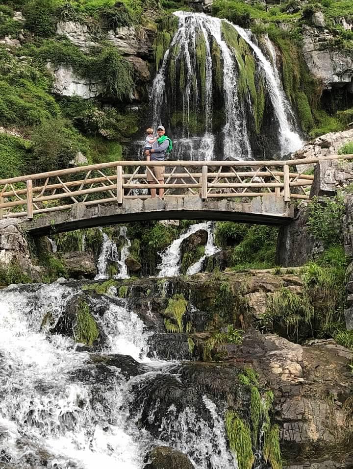 A family stands atop a bridge with a large waterfall behind it near Interlaken.