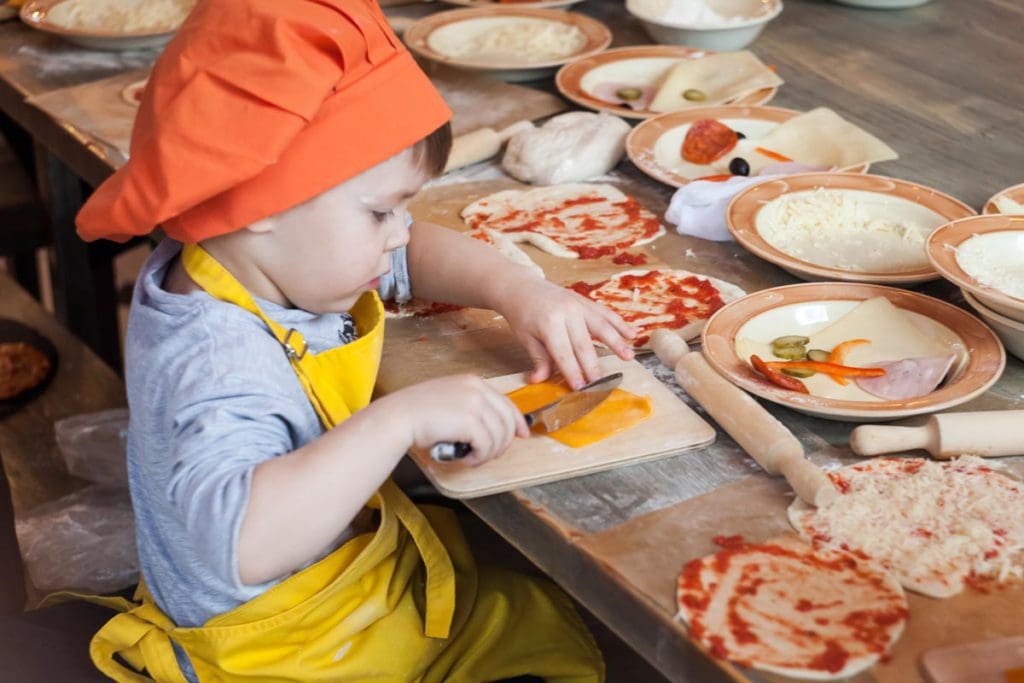A young child cuts a piece of cheese, while taking a cooking lesson in Florence with their family.
