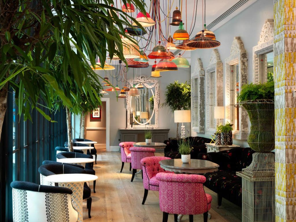 Inside the Orangery at the Ham Yard Hotel, Firmdale Hotels, featuring large, plush pink chairs and intimate seating arrangements in a light and airy dining room.