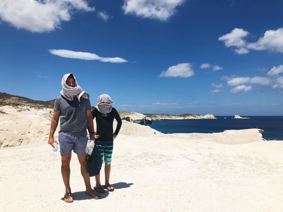 A dad and his son stand together on a rock ledge in Milos, overlooking an ocean view.