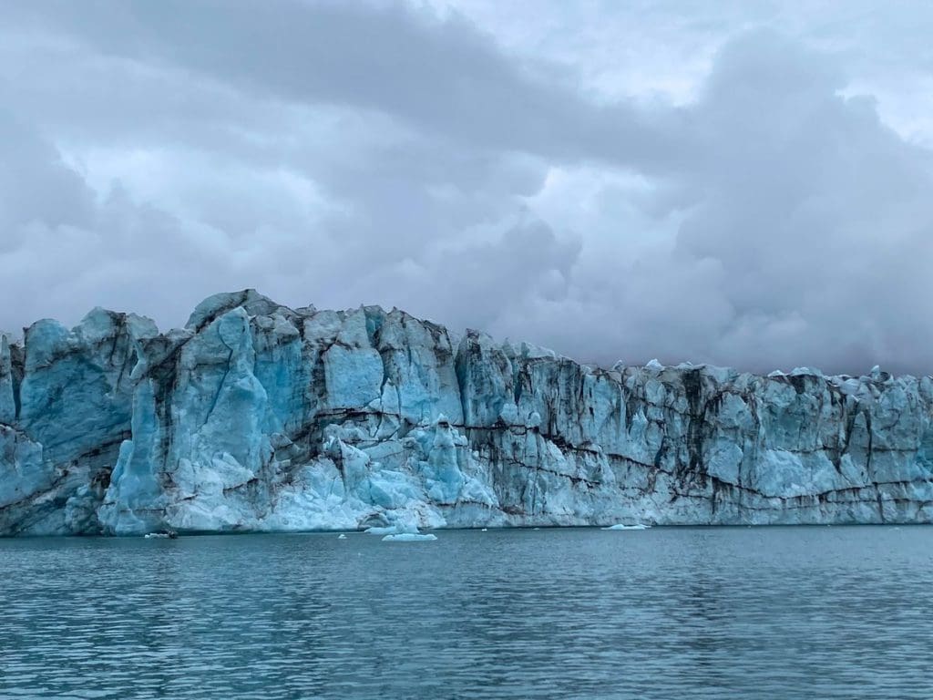 A glacier in Iceland rests along the edge of a body of water. Seeing glaciers is a must stop on this Iceland itinerary for families.