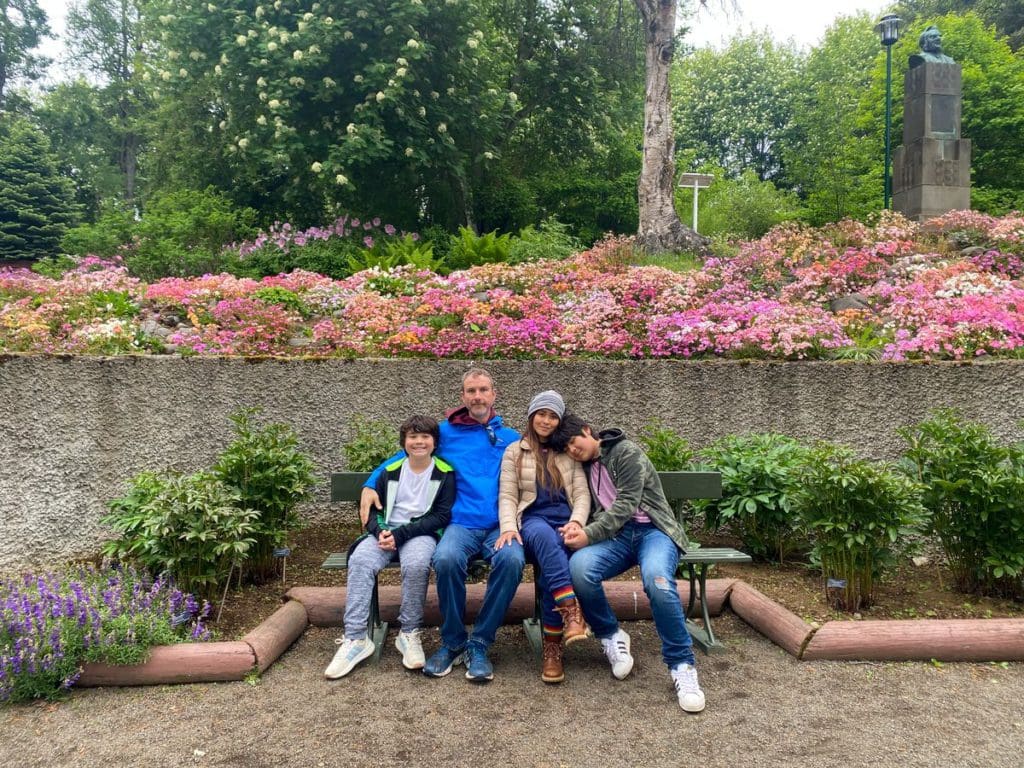 A family of four sits together on a bench in front of blooming flowers at Akureyri Botanical Garden, a must stop on this Iceland itinerary for families.