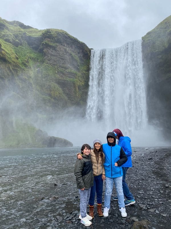 A family of four stands together in front of a waterfall in Iceland.