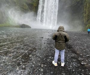 A man with his back turned stands in front of an Icelandic waterfall.