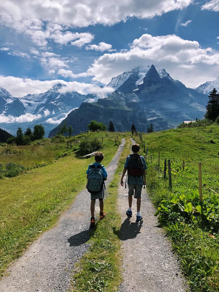 Two boys walk along a dirt path towards the mountains near Mürren, one of the best towns and villages to visit with your family in Switzerland.