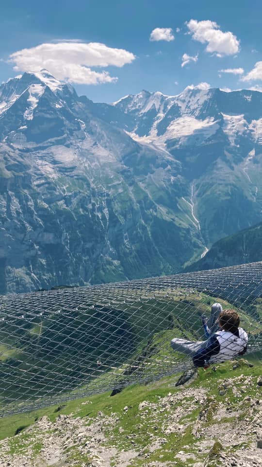 A man sits in a mesh chair overlooking a mountains view near Murren.