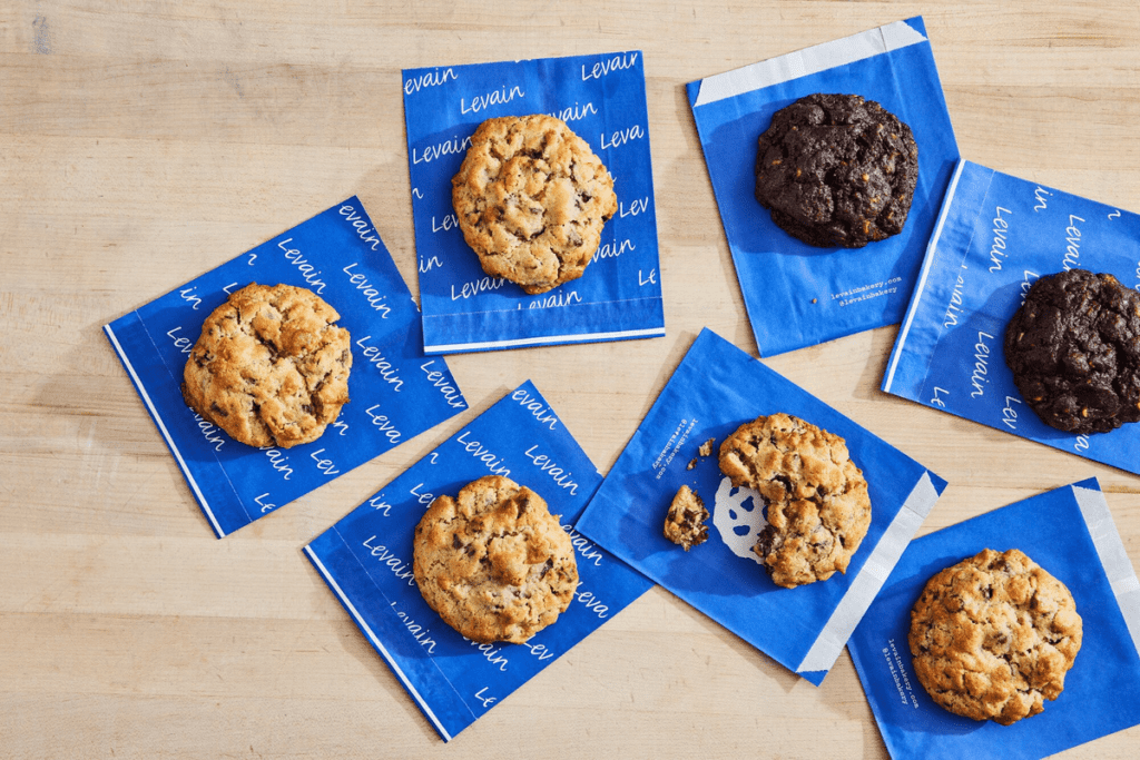 A table filled with cookies from Levain Bakery, including chocolate chip and chocolate options.