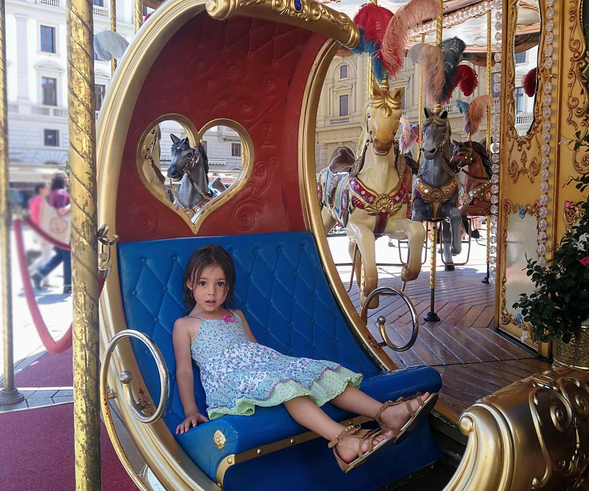 A young girl sits in a carousel seat in Piazza della Repubblica, one of the best places to visit on a Florence itinerary for families! 