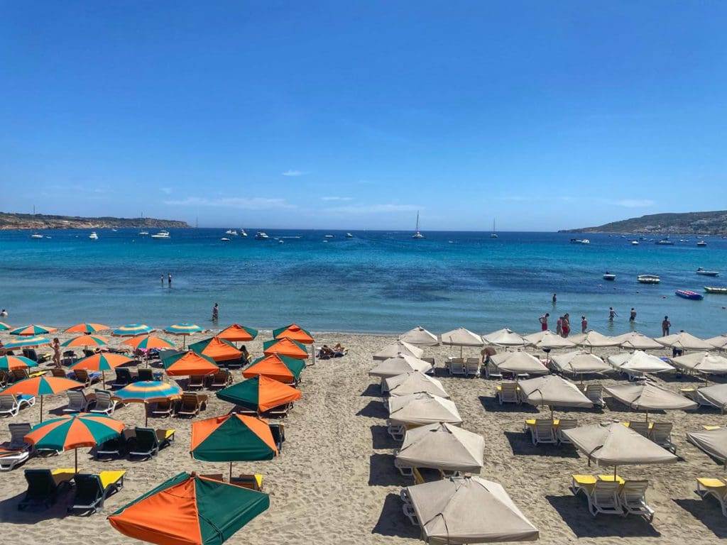 Several colorful umbrellas are lined on a beach in Malta, facing the blue sea, visiting the beach is this is one of our best tips for visiting Malta with kids.