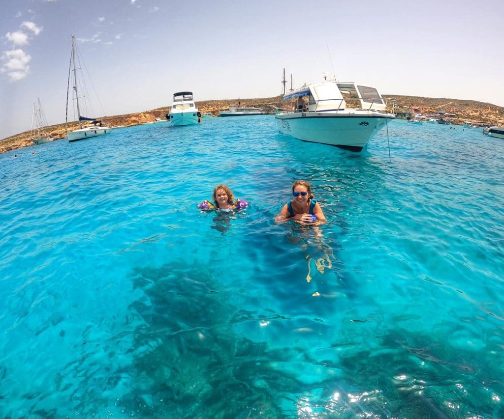 A mom and her young daughter swim in crystal blue waters near a boat off-shore in Malta.