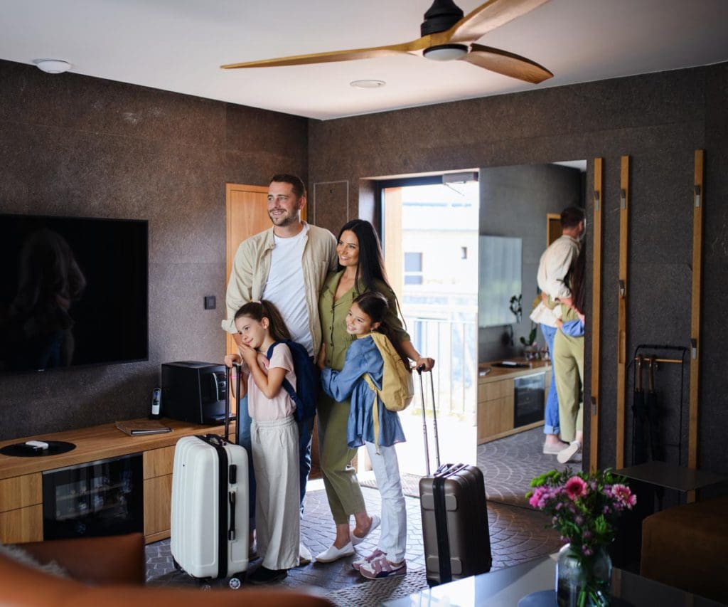 A family of four stands together in the entrance of a home rental with their luggage.