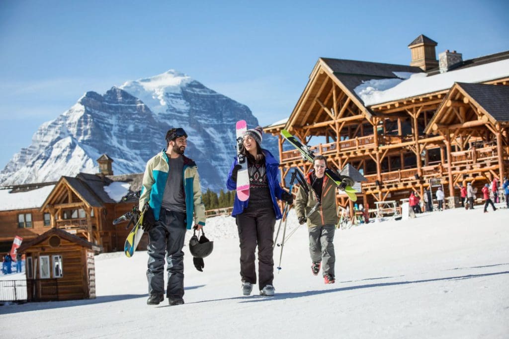 Three people holding ski gear walk across the snow in Banff, one of the best Thanksgiving destinations in the United States for families.