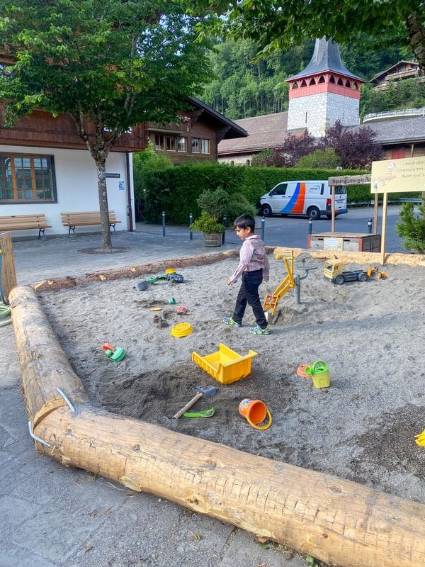 A young boy walks across a sandy playground area in Switzerland.