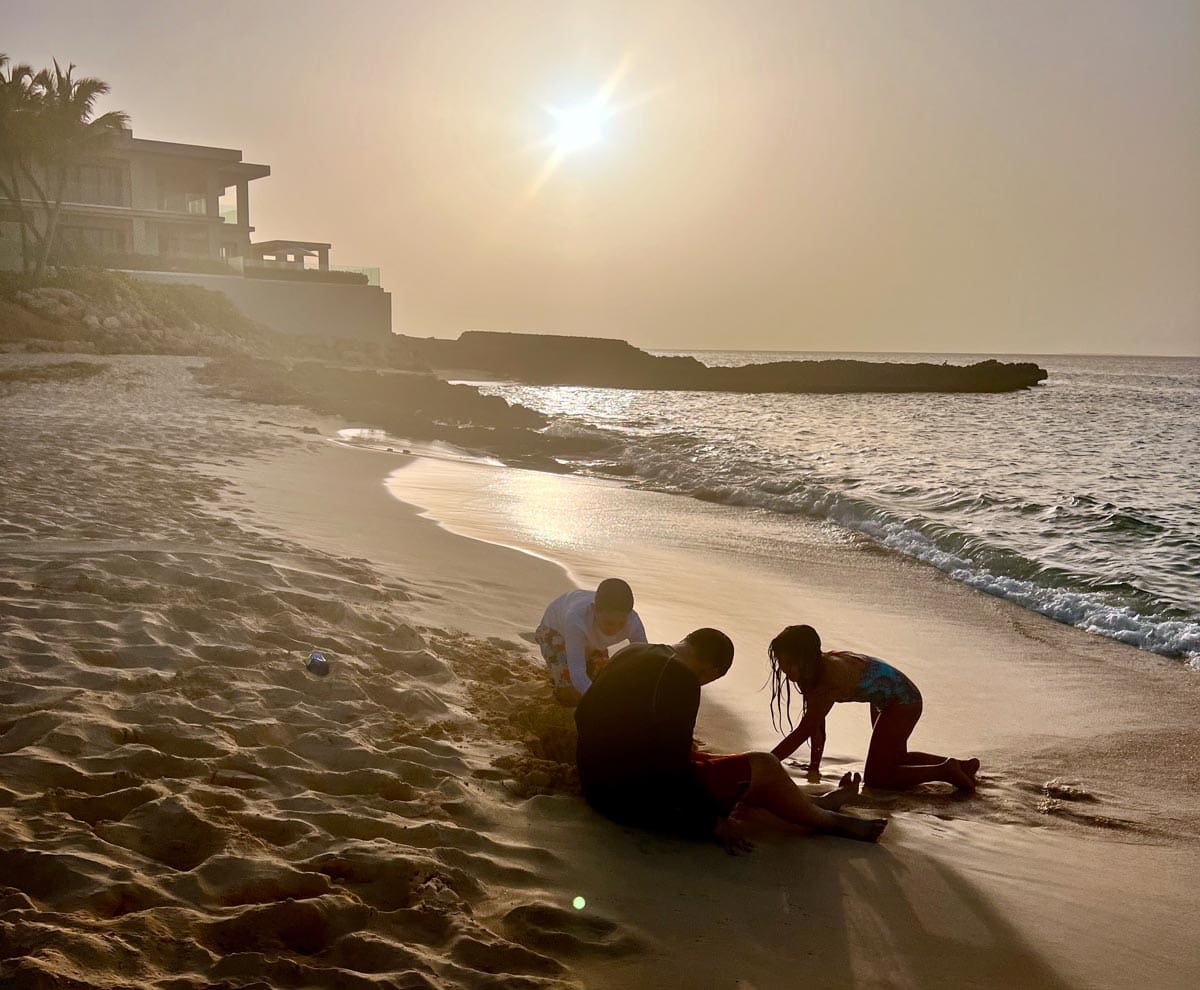 Two kids play with their dad on the sand along the ocean at Four Seasons Resort and Residences Anguilla.