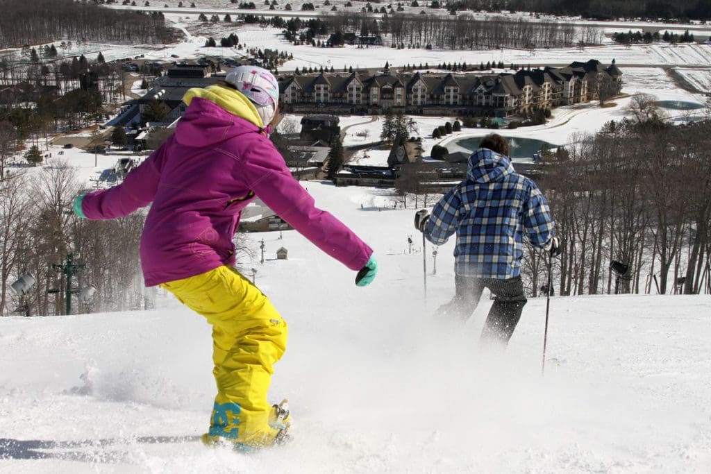 A woman and a man ski down a hill at Boyne Mountain Resort, one of the best budget-friendly Christmas destinations in the US for families.