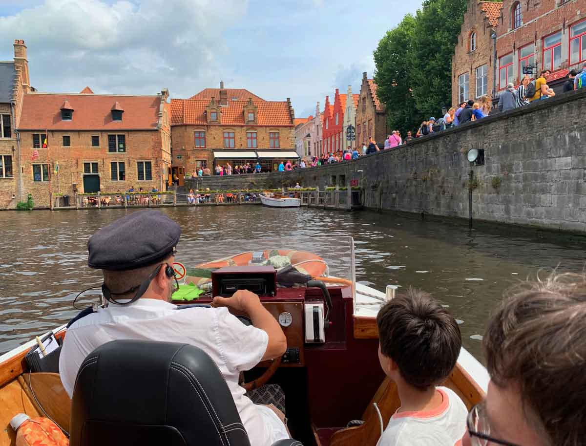 A young boy sits behind a boat driver, while exploring a canal in Bruges, one of the best places in Belgium for families.