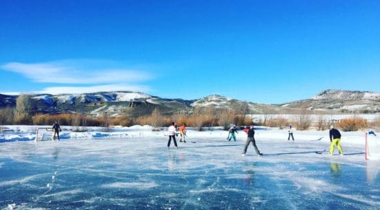 Several people ice skating on a frozen lake on a sunny, winter day at C Lazy U Ranch