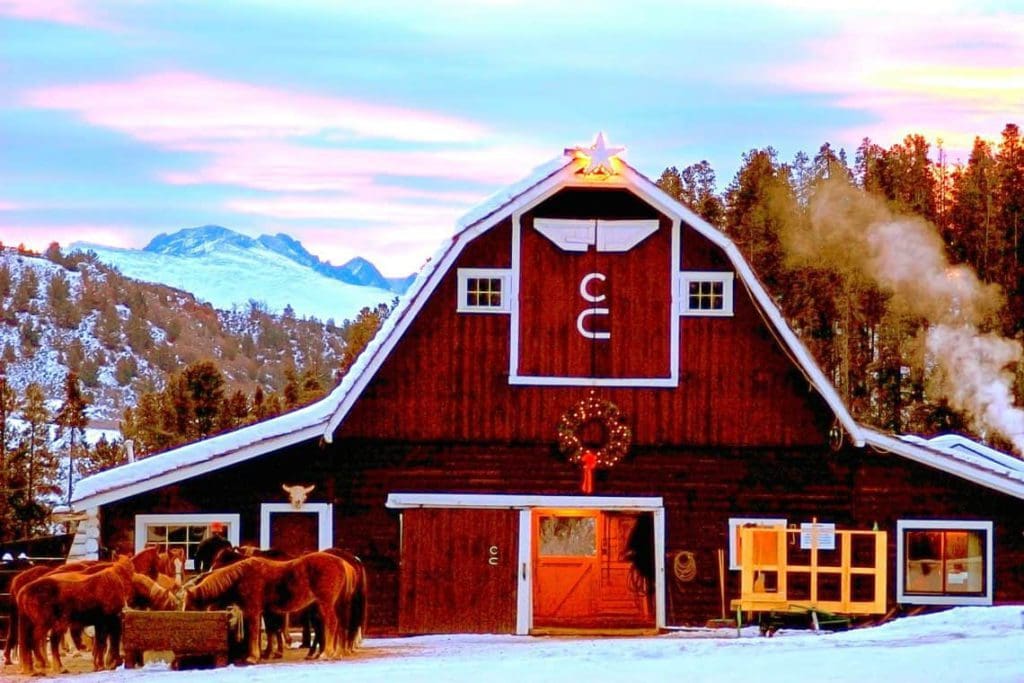 The exterior of the main barn at C Lazy U Ranch, decorated for Christmas, with horses out front, one of the best weekend getaways near Denver for families.