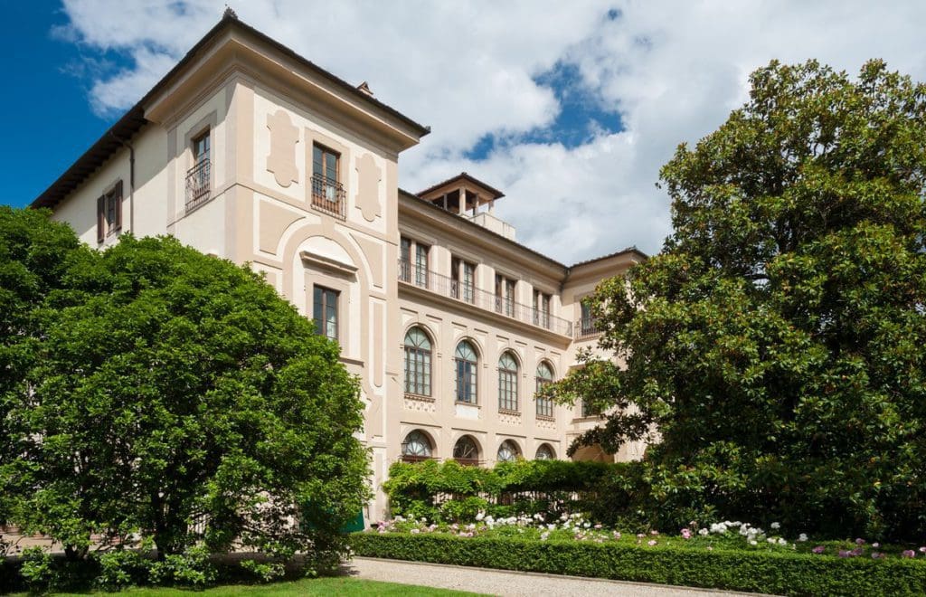 The grand exterior to Four Seasons Hotel Firenze, with large trees flanking the entrance. This is one of the best places to stay on a Florence itinerary for families. 