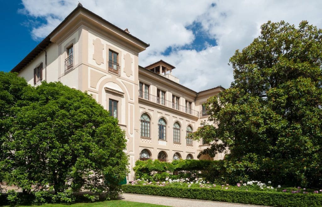 The grand exterior to Four Seasons Hotel Firenze, with large trees flanking the entrance. This is one of the best places to stay on a Florence itinerary for families.