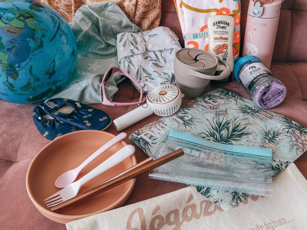 Several items laid out to be packed for a European beach vacation, including sunscreen, snacks, toys, and a handheld fan.