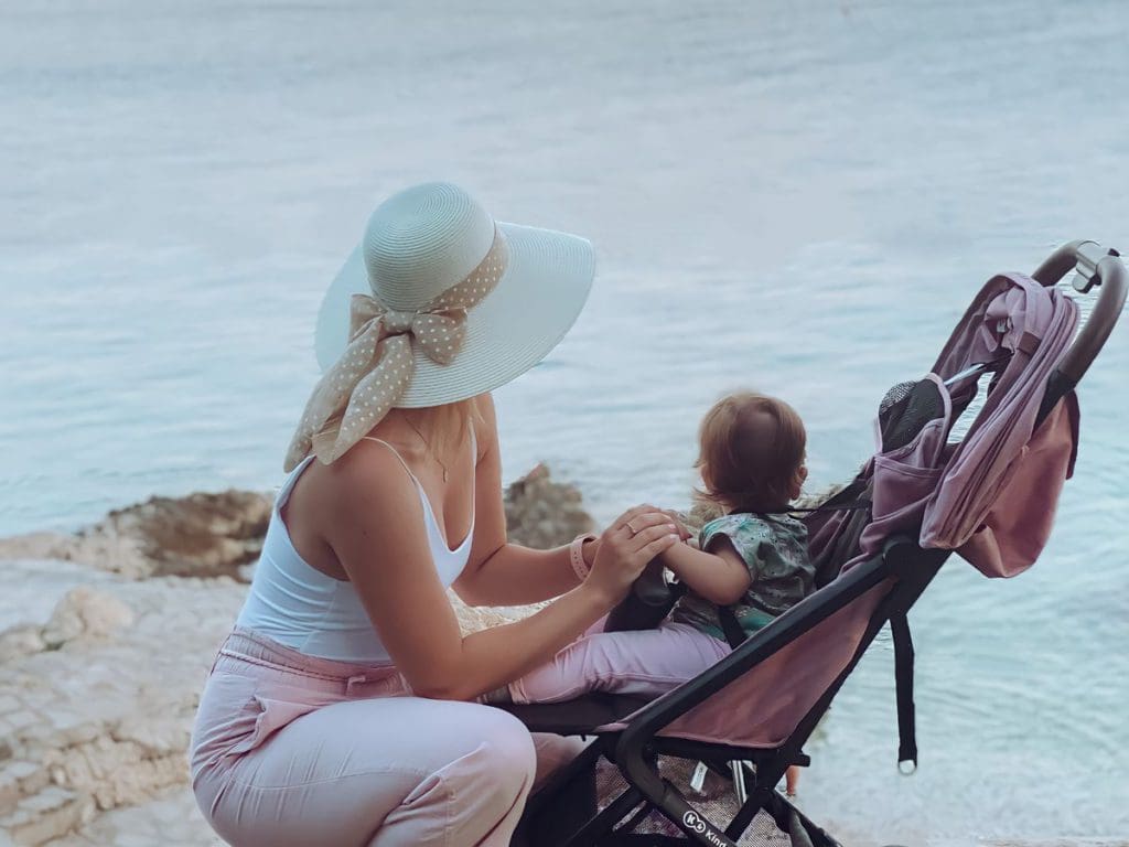 A mom crouches near her daughter, who is sitting in a stroller, to take in a view togehter.